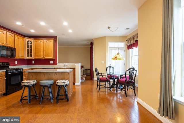 kitchen with a breakfast bar, light wood-style floors, a center island, black appliances, and brown cabinetry