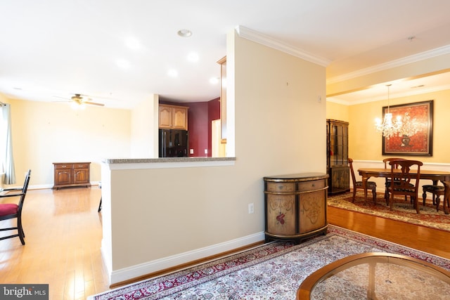 interior space featuring crown molding, ceiling fan with notable chandelier, baseboards, and light wood-style floors