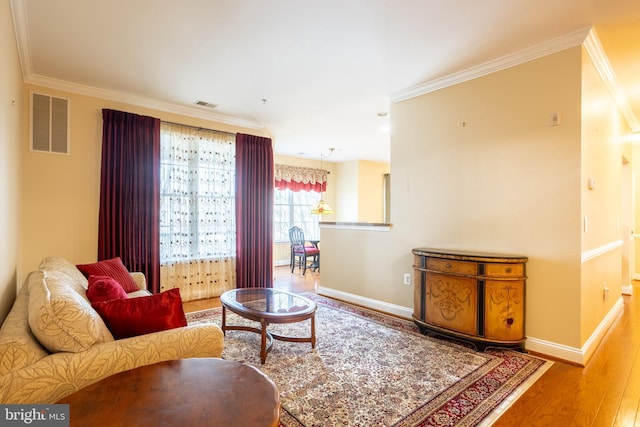 living area with baseboards, wood finished floors, visible vents, and crown molding