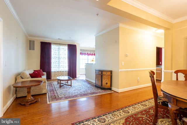 living area with baseboards, wood finished floors, visible vents, and crown molding