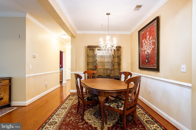 dining area with baseboards, visible vents, ornamental molding, wood finished floors, and a notable chandelier