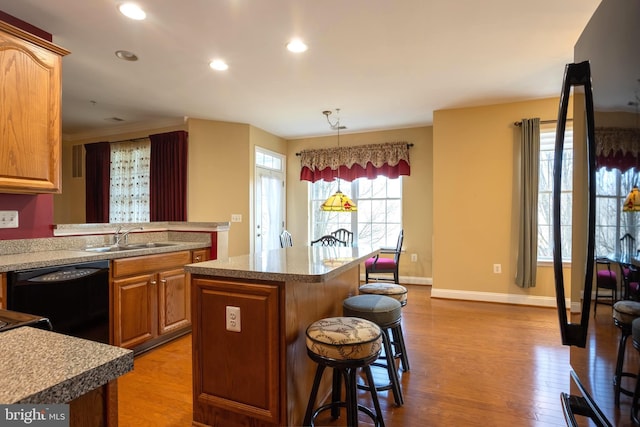 kitchen with dishwasher, a breakfast bar area, a center island, light wood-type flooring, and a sink