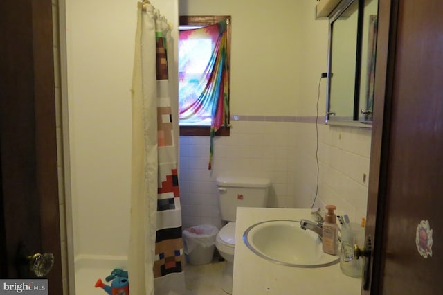 full bath with toilet, a wainscoted wall, a sink, curtained shower, and tile walls