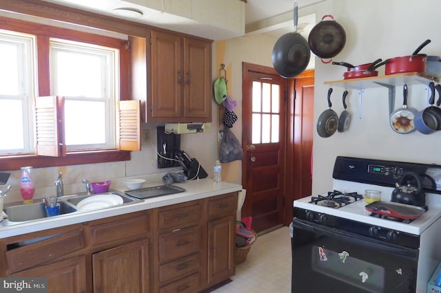 kitchen featuring range with gas cooktop, brown cabinets, a sink, light countertops, and backsplash