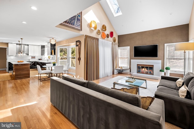 living room with light wood-type flooring, a glass covered fireplace, vaulted ceiling with skylight, and recessed lighting