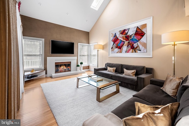 living area featuring a skylight, high vaulted ceiling, wood finished floors, and a glass covered fireplace