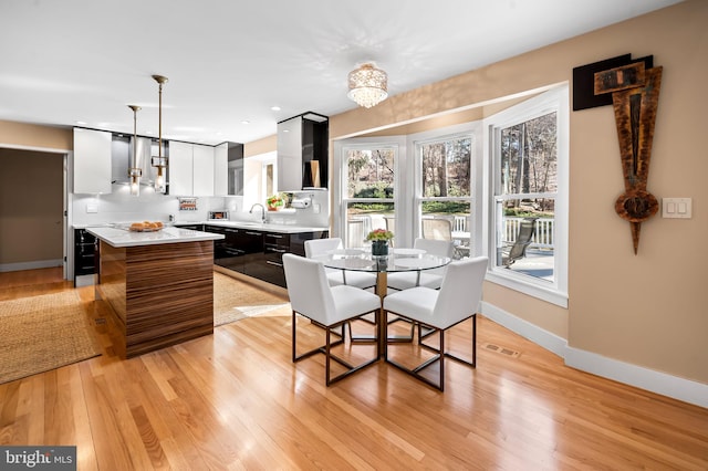 dining room with light wood-style flooring, a notable chandelier, beverage cooler, visible vents, and baseboards