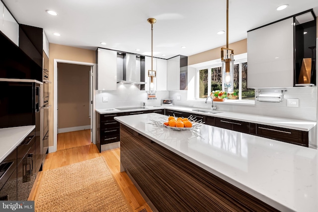 kitchen with light wood-style flooring, a sink, wall chimney exhaust hood, tasteful backsplash, and modern cabinets