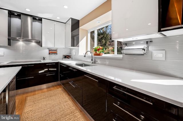 kitchen featuring light countertops, a sink, wall chimney range hood, modern cabinets, and stovetop