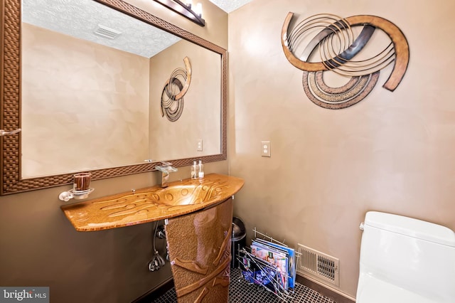 half bath featuring a textured ceiling, toilet, a sink, and visible vents