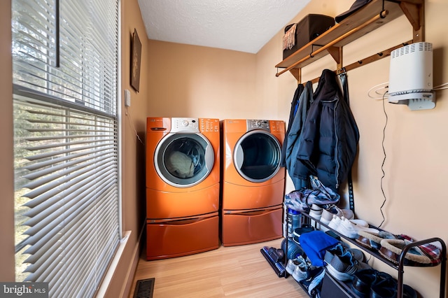 washroom with a textured ceiling, washing machine and dryer, laundry area, wood finished floors, and visible vents