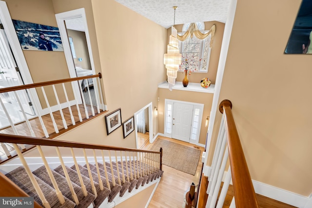 foyer featuring a textured ceiling, wood finished floors, a towering ceiling, baseboards, and stairway