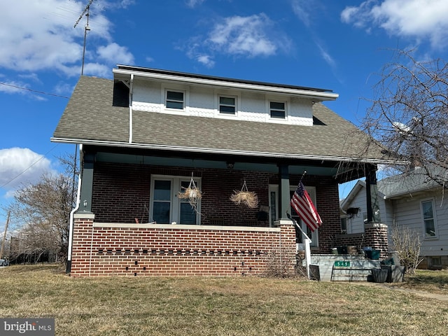 bungalow-style home with brick siding, covered porch, a front yard, and roof with shingles