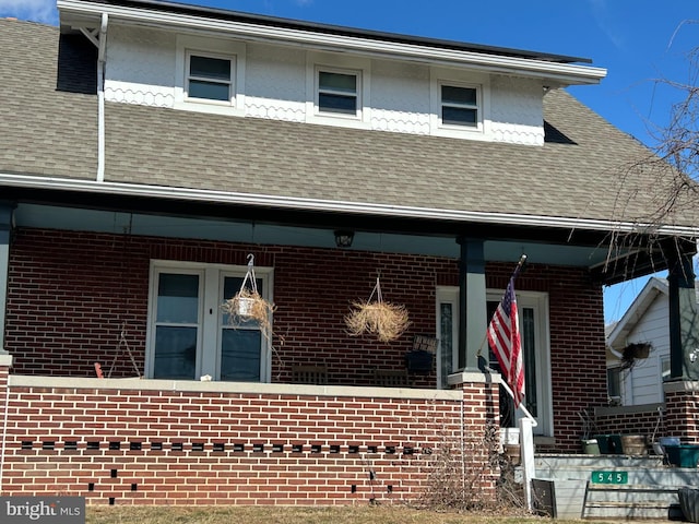 view of front of property featuring covered porch, brick siding, and roof with shingles