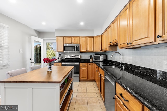 kitchen with light tile patterned floors, stainless steel appliances, decorative backsplash, a sink, and butcher block countertops