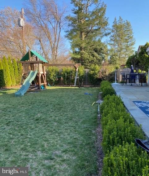 view of playground featuring a patio area, a lawn, and fence