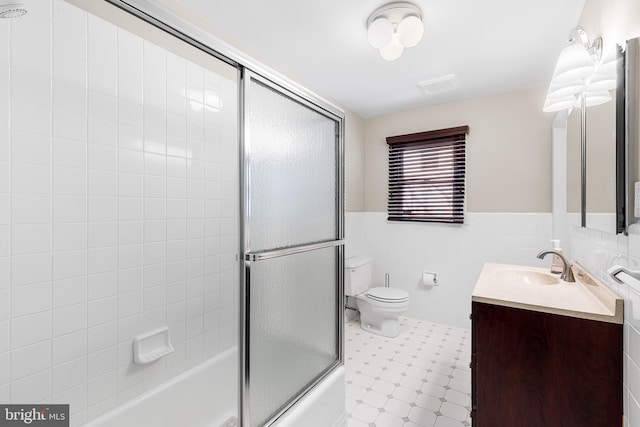 bathroom featuring shower / bath combination with glass door, tile walls, toilet, wainscoting, and vanity