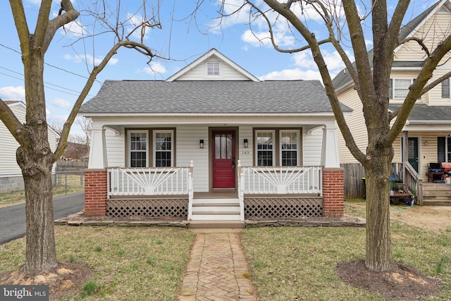 view of front of home with covered porch, roof with shingles, and a front lawn