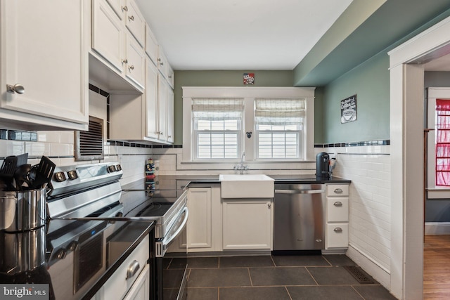 kitchen featuring dark countertops, stainless steel appliances, dark tile patterned floors, white cabinetry, and a sink