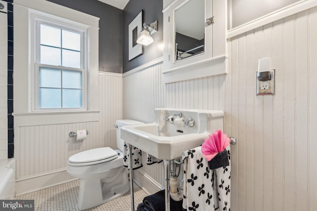 bathroom with wainscoting, toilet, a sink, tile patterned flooring, and a bath