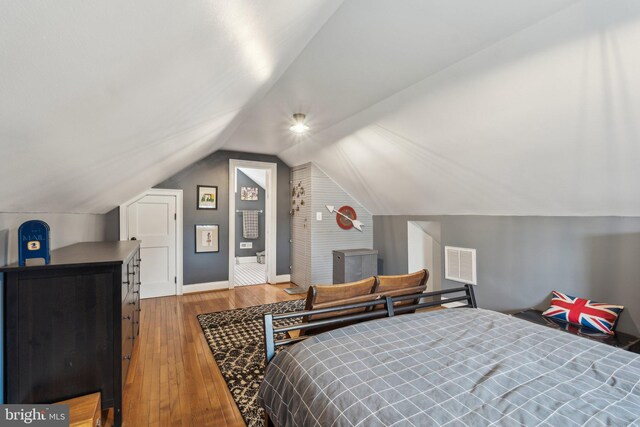 bedroom featuring vaulted ceiling, hardwood / wood-style floors, visible vents, and baseboards