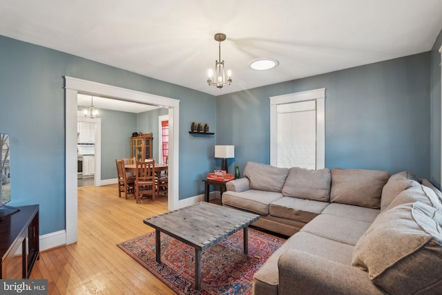 living room with a chandelier, light wood finished floors, and baseboards