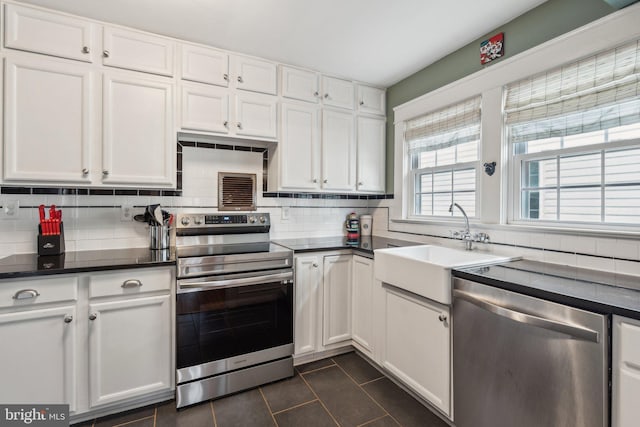 kitchen featuring tasteful backsplash, dark countertops, stainless steel appliances, white cabinetry, and a sink