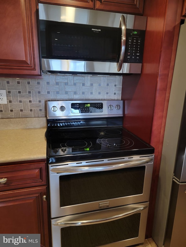 kitchen featuring reddish brown cabinets, light countertops, appliances with stainless steel finishes, and backsplash