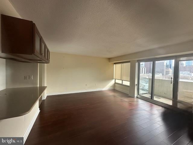 unfurnished living room with a textured ceiling, dark wood finished floors, and baseboards