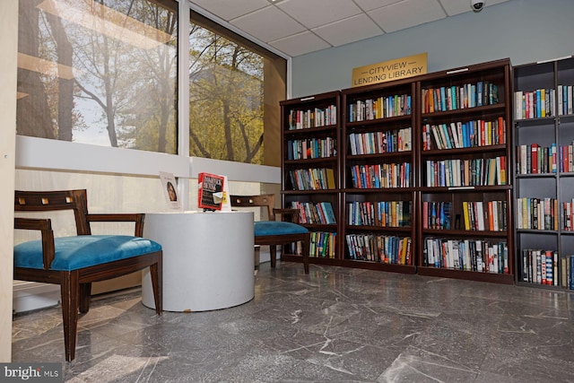 living area featuring a wall of windows, marble finish floor, and a drop ceiling