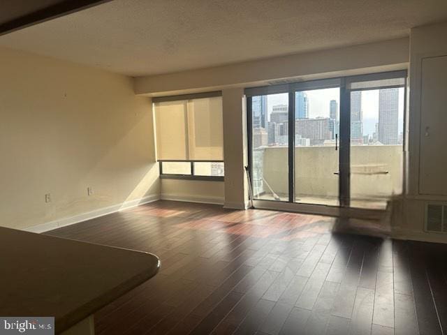 empty room with dark wood-type flooring, visible vents, and baseboards