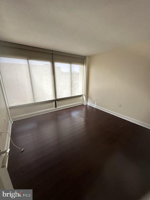 empty room with a textured ceiling, dark wood finished floors, and baseboards