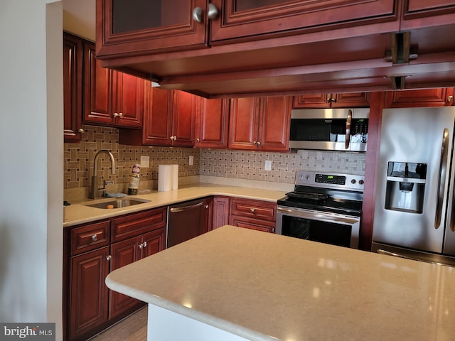 kitchen featuring reddish brown cabinets, stainless steel appliances, a sink, and light countertops