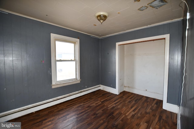 unfurnished bedroom featuring a baseboard heating unit, baseboards, wood finished floors, and crown molding