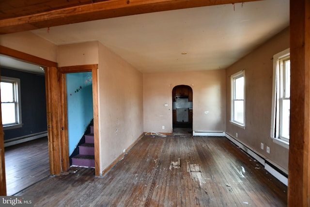 spare room with a baseboard heating unit, arched walkways, wood-type flooring, and stairs