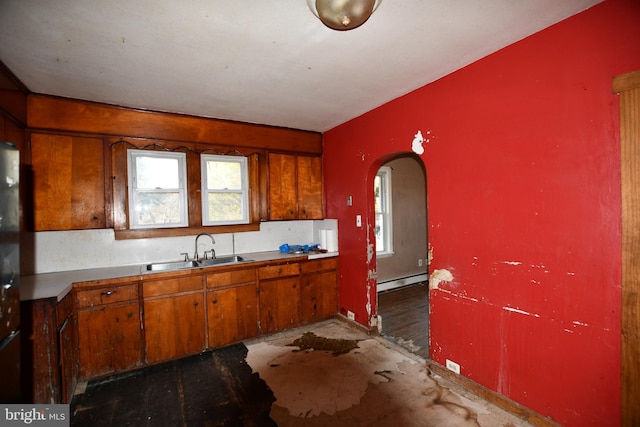 kitchen featuring arched walkways, a baseboard heating unit, brown cabinetry, and a sink