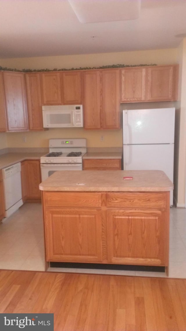 kitchen with light wood-type flooring, white appliances, a kitchen island, and light countertops