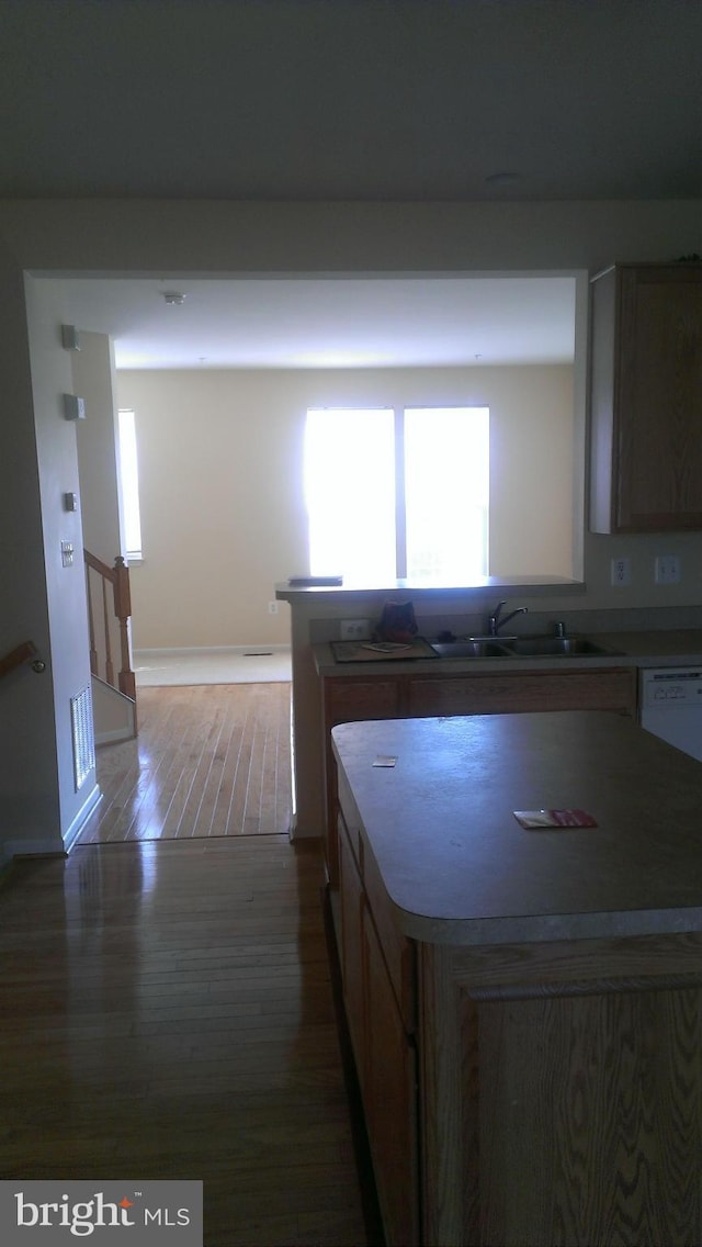 kitchen with a sink, light countertops, wood finished floors, and a center island