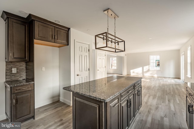 kitchen with open floor plan, dark brown cabinets, light wood-style flooring, and decorative backsplash