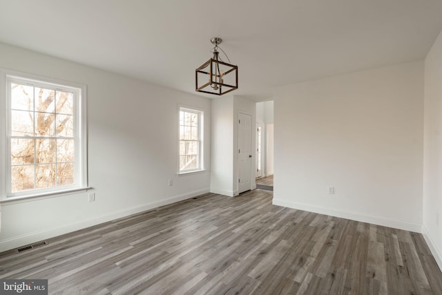 unfurnished dining area featuring an inviting chandelier, visible vents, baseboards, and wood finished floors