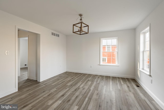 spare room with a notable chandelier, wood finished floors, visible vents, and baseboards