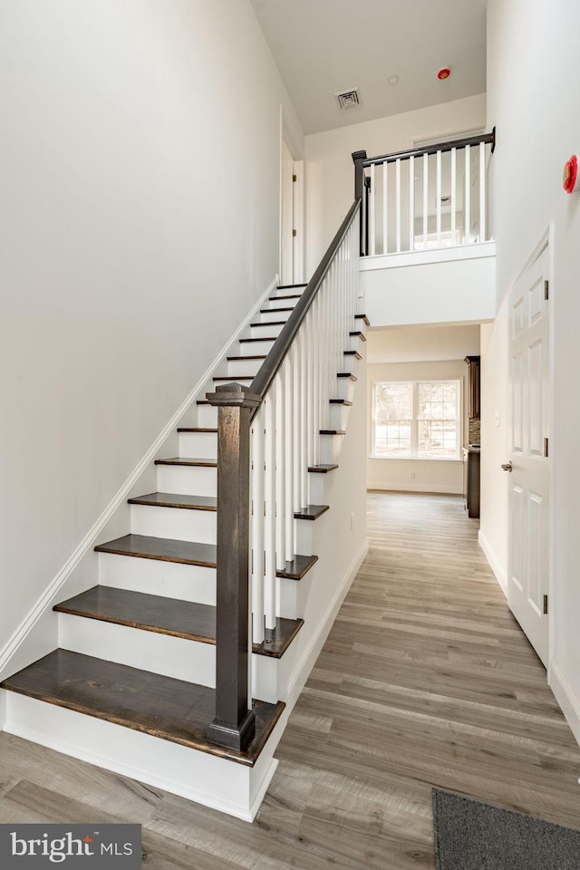 stairway with baseboards, visible vents, a high ceiling, and wood finished floors