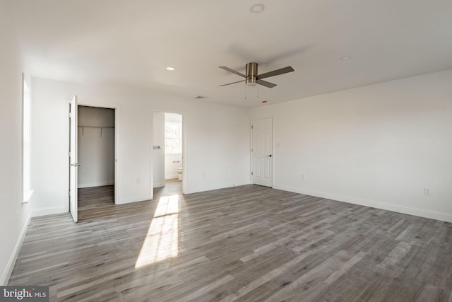 unfurnished bedroom with a closet, ensuite bathroom, a ceiling fan, wood finished floors, and baseboards