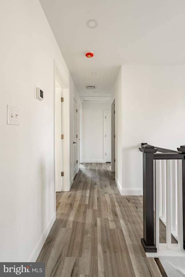 hallway featuring visible vents, baseboards, and wood finished floors