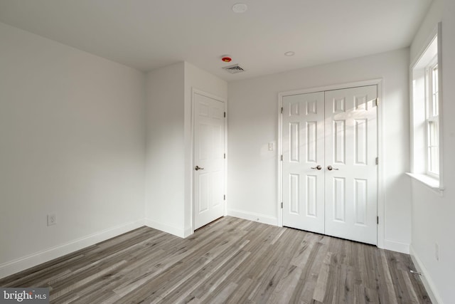 unfurnished bedroom featuring a closet, wood finished floors, visible vents, and baseboards