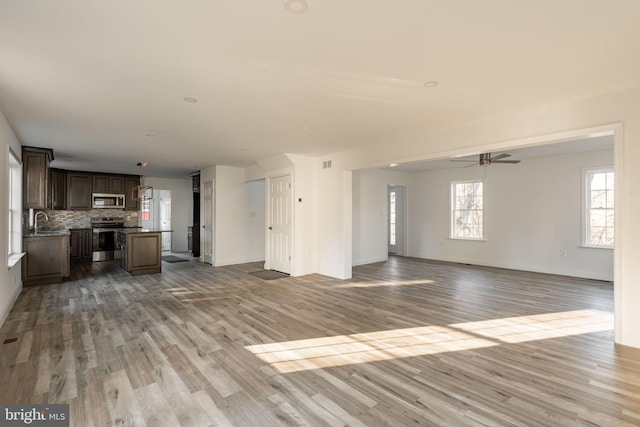 unfurnished living room featuring wood finished floors, a sink, a ceiling fan, and baseboards