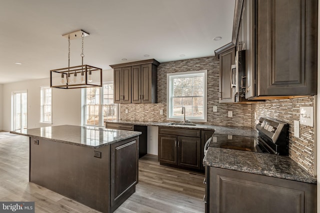 kitchen featuring light wood-style floors, a kitchen island, dark stone counters, and a sink