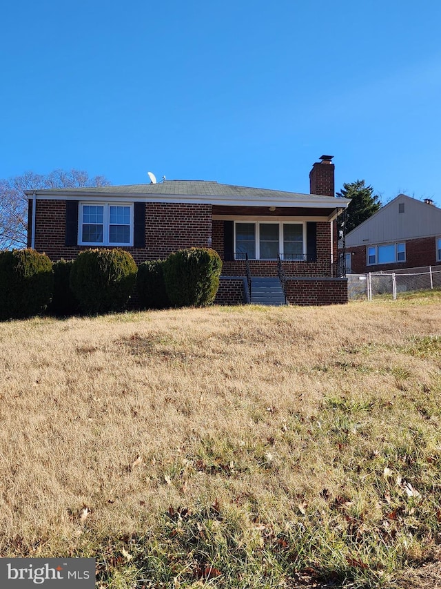 ranch-style house with a chimney, fence, a front lawn, a porch, and brick siding