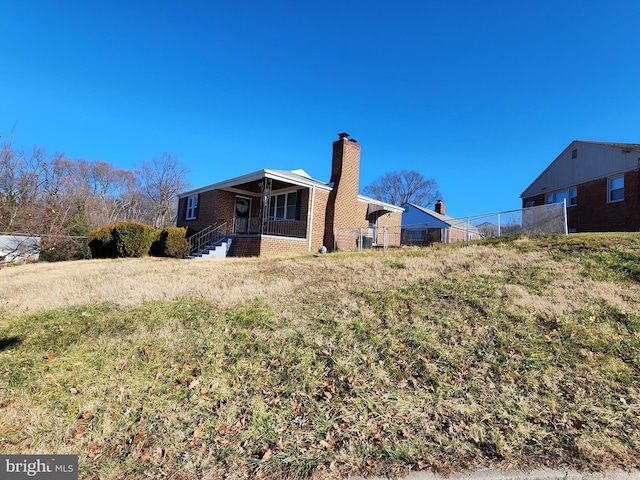 view of side of property featuring brick siding, a chimney, and fence