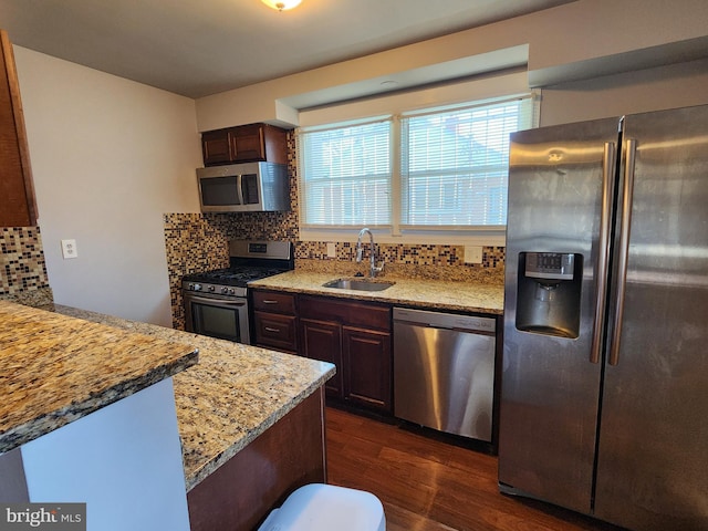 kitchen with appliances with stainless steel finishes, dark wood-type flooring, a sink, and tasteful backsplash